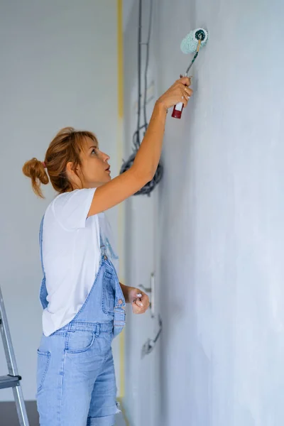 young beautiful woman makes repairs in the apartment, paints the walls with a roller. Molar work.