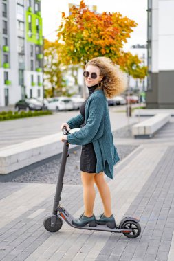 İşe elektrikli scooterla giden genç, güzel bir kadın, modern kız, yeni nesil, elektrik nakli, ekolojik ulaşım, ekolojik ulaşım, gün batımı