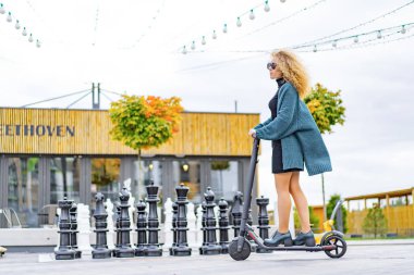 İşe elektrikli scooterla giden genç, güzel bir kadın, modern kız, yeni nesil, elektrik nakli, ekolojik ulaşım, ekolojik ulaşım, gün batımı