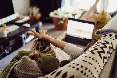 Kadın elinde dizüstü bilgisayarla kanepede yatıyor. İzolasyonda zaman geçirmek. Evden bir dizüstü bilgisayarla çalışıyorum..