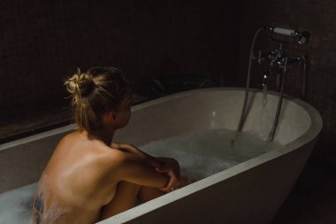 Güzel gülümseyen beyaz kadın banyoda ıslak saçlarıyla poz veriyor, banyoda dinleniyor. Genç bir kadın küvette yatıyor..