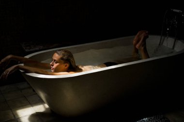 Güzel gülümseyen beyaz kadın banyoda ıslak saçlarıyla poz veriyor, banyoda dinleniyor. Genç bir kadın küvette yatıyor..