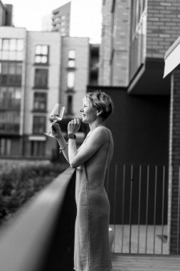 Terasta elinde bir bardak şarapla güzel bir kadın dinleniyor, gülüyor. siyah beyaz fotoğraf.