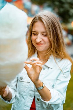 Kırmızı elbiseli ve beyaz kot ceketli güzel bir kadın bir eğlence parkında diş ipiyle.