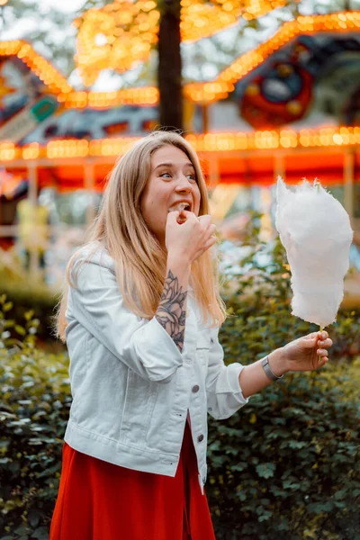 穿着红色衣服和白色斜纹棉布夹克的年轻貌美女人在一个有糖果牙线的游乐园里 — 图库照片