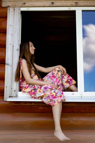 明るい色の太陽の下で長い髪の若い美しい女性が窓に座っています カントリースタイル — ストック写真
