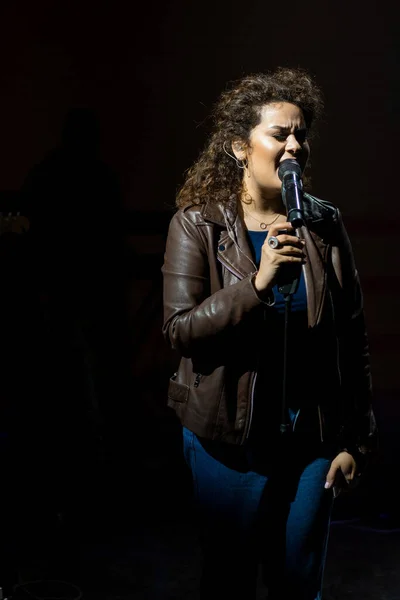Young woman singer on stage singing into a microphone, spotlights.