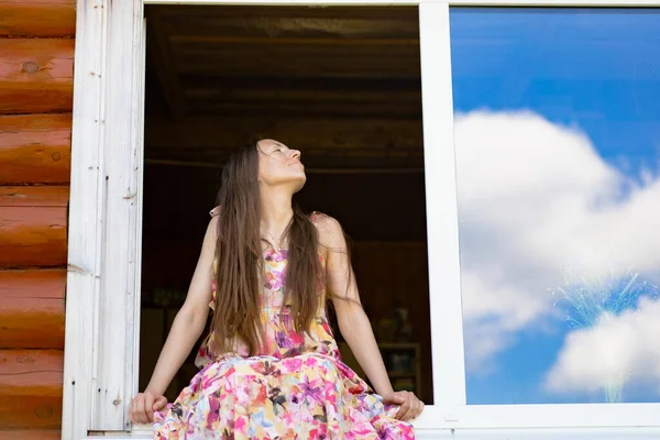 那个长头发 穿着鲜艳的太阳衣的年轻漂亮的女人坐在窗前 国家风格 — 图库照片