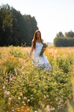 Çavdar ve buğday tarlaları arasında beyaz elbiseli, şapkalı, uzun saçlı genç ve güzel bir kadın. Kırsal tarzda uzun saçlı, çiçekli bir tarlada beyaz bir elbise giyen bir kavram.