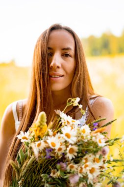 Çavdar ve buğday tarlaları arasında beyaz elbiseli, şapkalı, uzun saçlı genç ve güzel bir kadın. Kırsal tarzda uzun saçlı, çiçekli bir tarlada beyaz bir elbise giyen bir kavram.