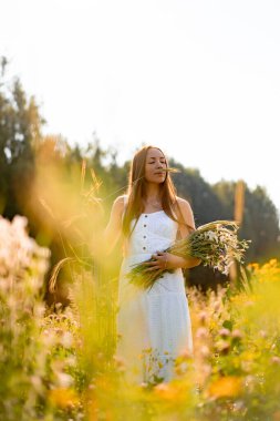 Çavdar ve buğday tarlaları arasında beyaz elbiseli, şapkalı, uzun saçlı genç ve güzel bir kadın. Kırsal tarzda uzun saçlı, çiçekli bir tarlada beyaz bir elbise giyen bir kavram.