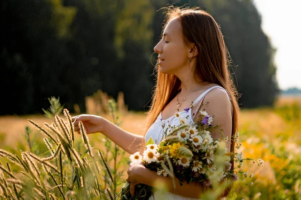 若い美しい女性は白いドレスと帽子で長い髪をウィットライ麦と小麦の黄色のフィールドの間で 開花場の白い太陽の下で長い髪の素朴なスタイルのコンセプト — ストック写真