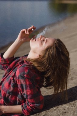 Genç bir kadın sahilde sigara içiyor.