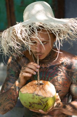 Hasır şapkalı genç yakışıklı adam taze hindistan cevizi içiyor. 