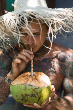 Hasır şapkalı genç yakışıklı adam taze hindistan cevizi içiyor. 