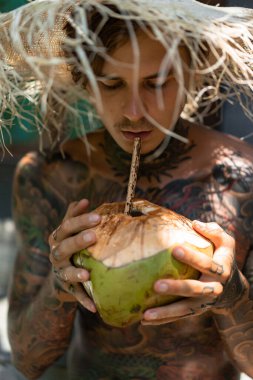Hasır şapkalı genç yakışıklı adam taze hindistan cevizi içiyor. 