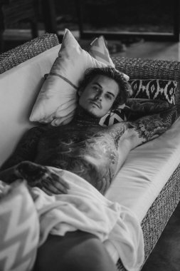 Dövmeli yakışıklı genç adam oturma odasında dinleniyor.