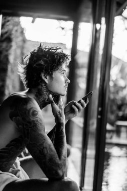 Dövmeli yakışıklı genç adam telefonda hoparlörden konuşuyor.