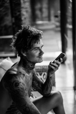 Dövmeli yakışıklı genç adam telefonda hoparlörden konuşuyor.