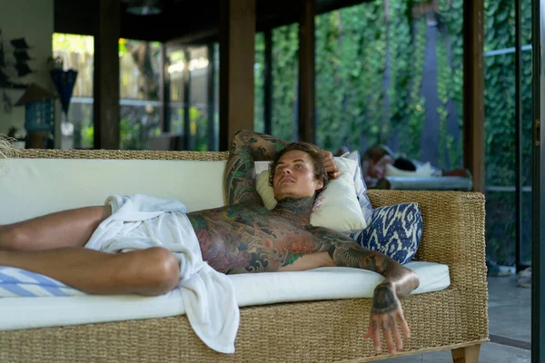 handsome young man in tattoos is resting in the living room