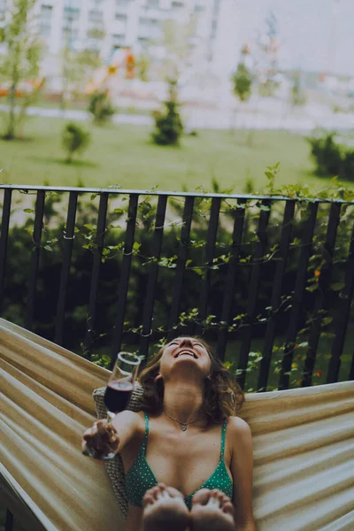 A young woman on a private terrace of a country house in a hammock is resting, a glass of champagne lambrusca in her hand, summer chill.