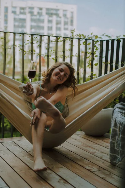 A young woman on a private terrace of a country house in a hammock is resting, a glass of champagne lambrusca in her hand, summer chill.