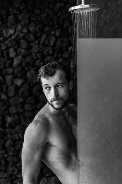 Adam duş alıyor, saçlarını şampuan ürünüyle yıkıyor.