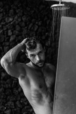 Adam duş alıyor, saçlarını şampuan ürünüyle yıkıyor.
