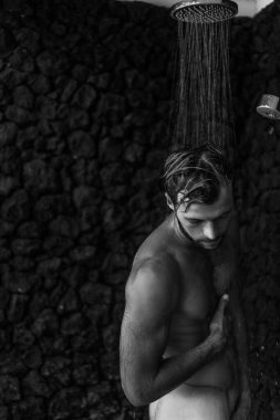 Adam duş alıyor, saçlarını şampuan ürünüyle yıkıyor.