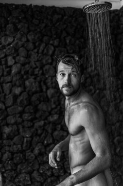 Adam duş alıyor, saçlarını şampuan ürünüyle yıkıyor.