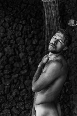 Adam duş alıyor, saçlarını şampuan ürünüyle yıkıyor.