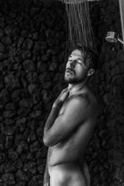 Adam duş alıyor, saçlarını şampuan ürünüyle yıkıyor.