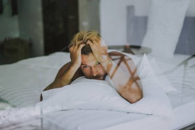 Seksi çıplak genç adam yatakta yatarken kameraya bakıyor. Ka