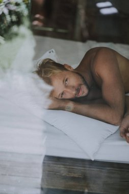 Seksi çıplak genç adam yatakta yatarken kameraya bakıyor. Ka
