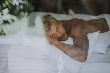 Seksi çıplak genç adam yatakta yatarken kameraya bakıyor. Ka