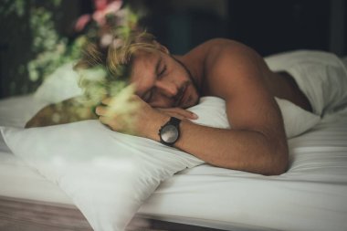 Seksi çıplak genç adam yatakta yatarken kameraya bakıyor. Ka