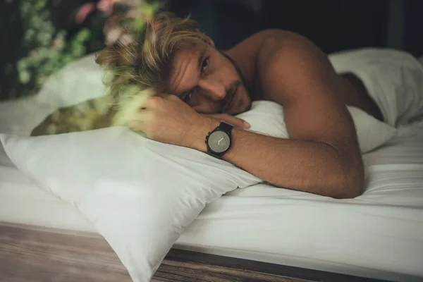 ベッドに寝そべっている間にセクシーな裸の若い男がカメラを見ている — ストック写真