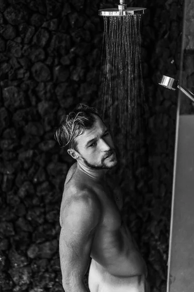 Adam duş alıyor, saçlarını şampuan ürünüyle yıkıyor.
