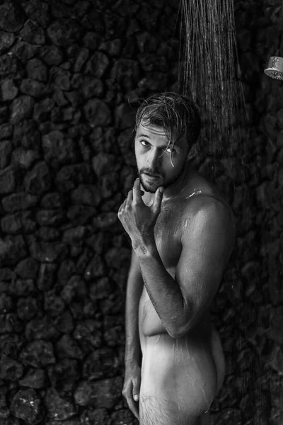 Adam duş alıyor, saçlarını şampuan ürünüyle yıkıyor.