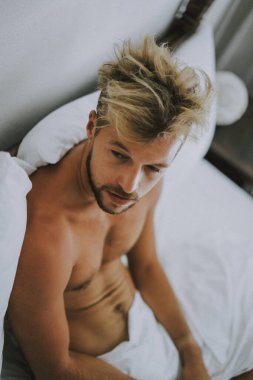 Seksi çıplak genç adam yatakta yatarken kameraya bakıyor. Ka