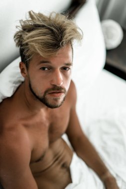Seksi çıplak genç adam yatakta yatarken kameraya bakıyor. Ka