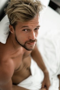 Seksi çıplak genç adam yatakta yatarken kameraya bakıyor. Ka
