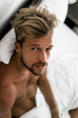 Seksi çıplak genç adam yatakta yatarken kameraya bakıyor. Ka