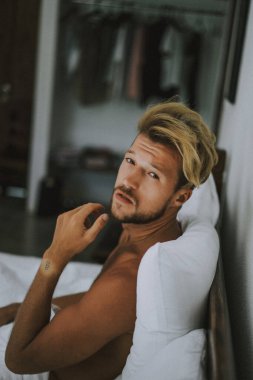 Seksi çıplak genç adam yatakta yatarken kameraya bakıyor. Ka