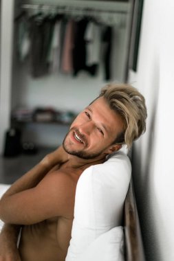 Seksi çıplak genç adam yatakta yatarken kameraya bakıyor. Ka