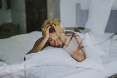 Seksi çıplak genç adam yatakta yatarken kameraya bakıyor. Ka