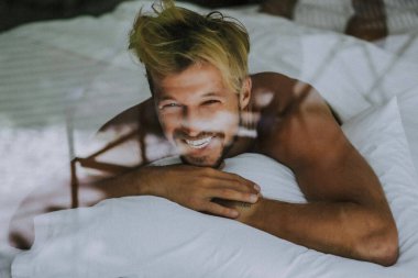 Seksi çıplak genç adam yatakta yatarken kameraya bakıyor. Ka