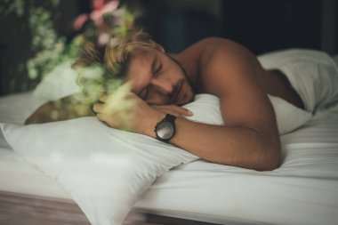 Seksi çıplak genç adam yatakta yatarken kameraya bakıyor. Ka