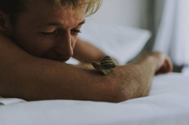 Seksi çıplak genç adam yatakta yatarken kameraya bakıyor. Ka