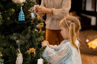 Anne ve çocuklar Noel ağacını çelenkler ve oyuncaklarla süsler. Aile Noel ağacını süslüyor. Noel ve Yeni Yıl için hazırlanıyorum. Çocuklar ağaca sevinir..